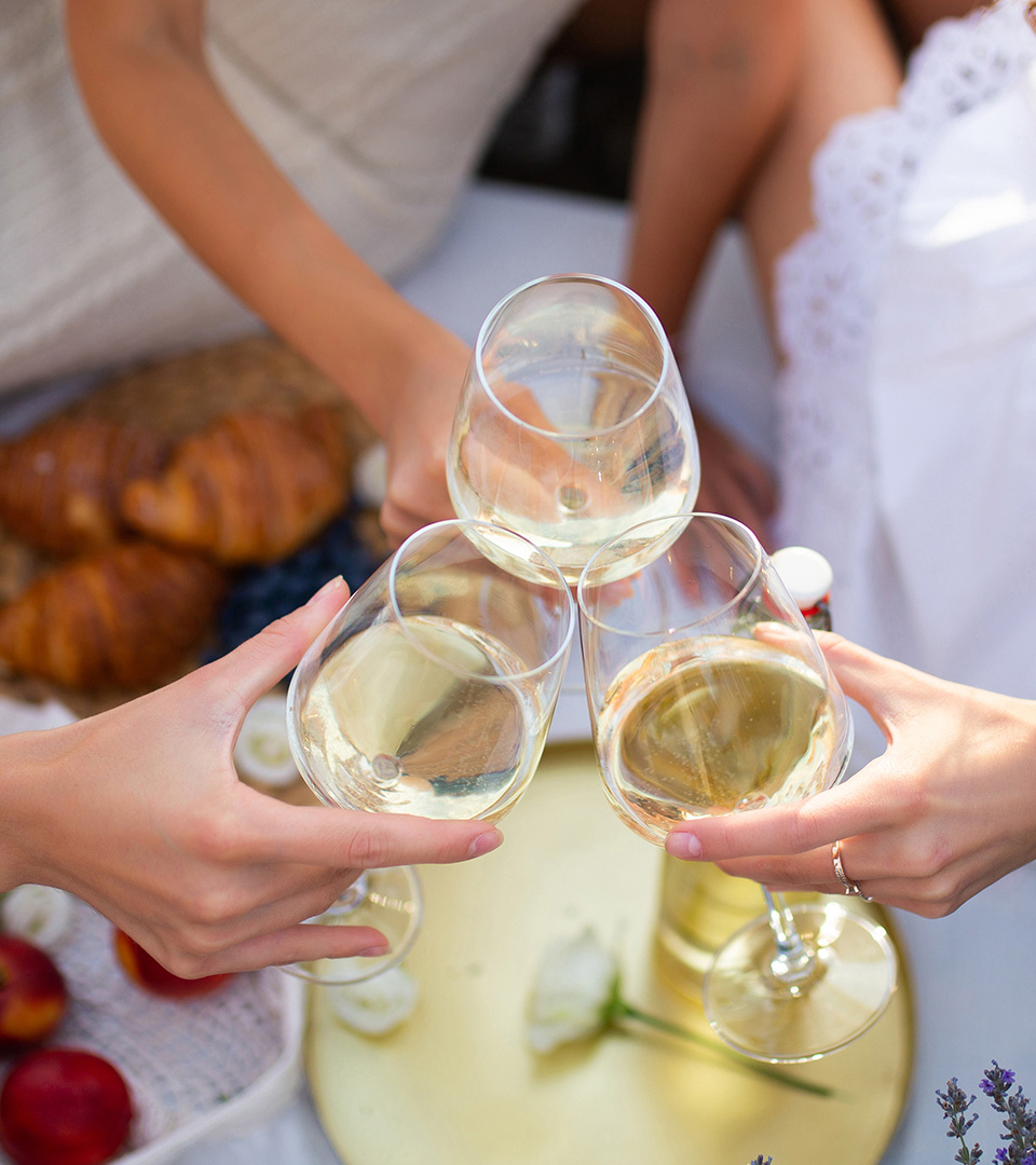 Photo vu d'en haut, trois femme qui trinquent avec un verre de blanc pétillant dans les mains au dessus d'un brunch.