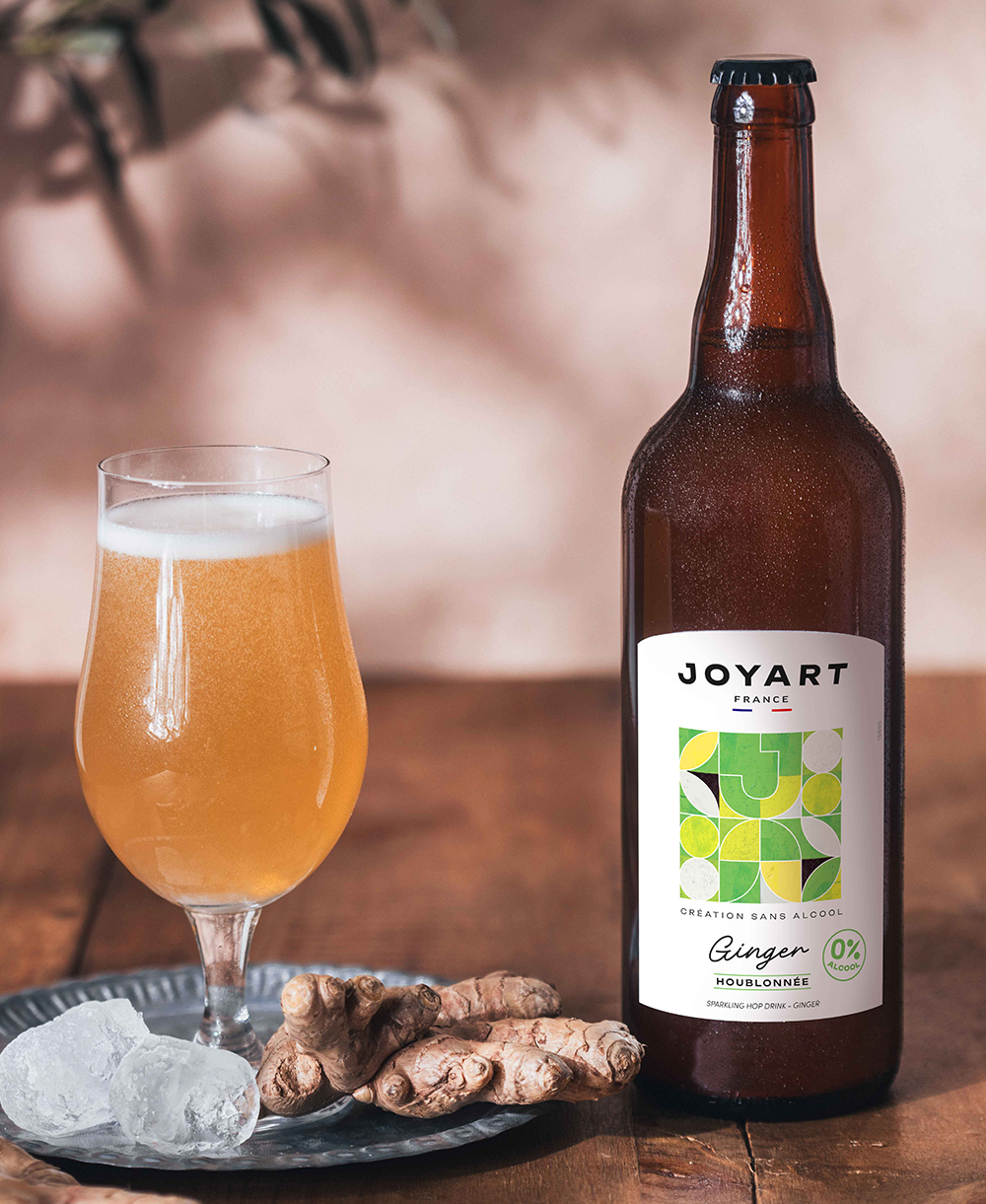 Photo d'ambiance de notre référence houblonnée Ginger posé sur une table en bois rustique avec à gauche un verre remplie sur une assiette avec deux glaçon et du gingembre.